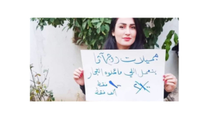 مديرة مجموعة "جميلات روج آفا" هيلين عثمان وهي تحمل لافتة عن الحملة التي قمن بها لتقديم بعض الحاجيات بسعر تفضيلي بهدف كسر الاحتكار. الصورة من الفيس بوك.